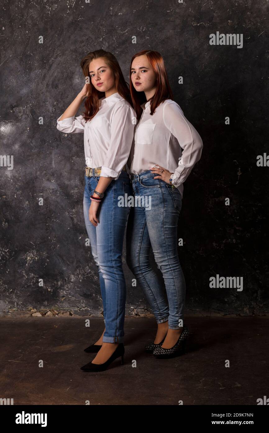Beautiful teen girls dressed in white shirt and blue jeans standing close to each other studio portrait Stock Photo