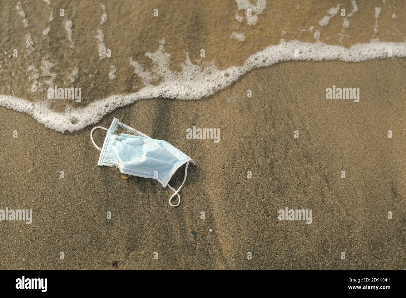 Medical face mask discarded on sea tar polluted shore,covid19 disease pollution Stock Photo