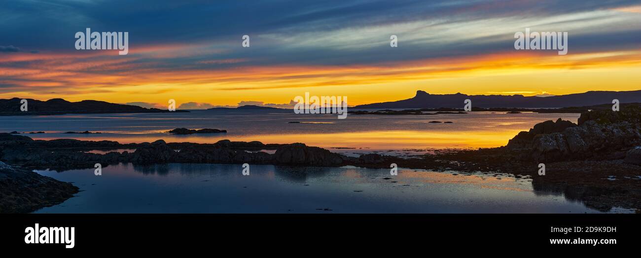 Sunset over the Isle of Eigg in the Small Isles, viewed from the Rhu Peninsula, Arisaig, Lochaber, Highland, Scotland.  Panoramic. Stock Photo