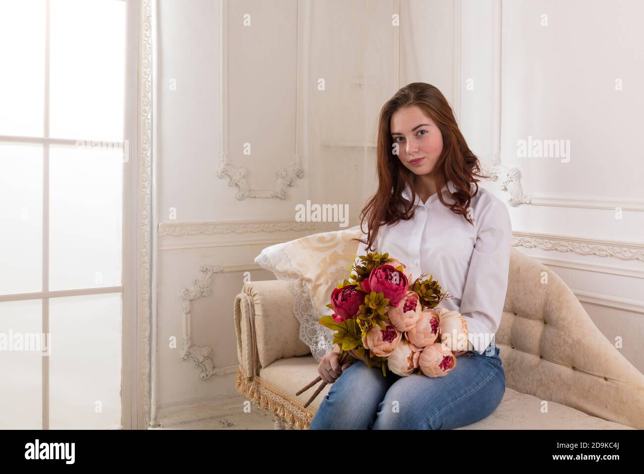 Beautiful young girl sitting on sofa with flowers Stock Photo - Alamy