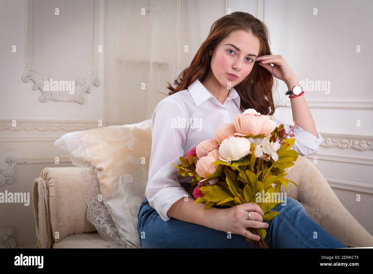 Beautiful young girl sitting on sofa with flowers Stock Photo - Alamy