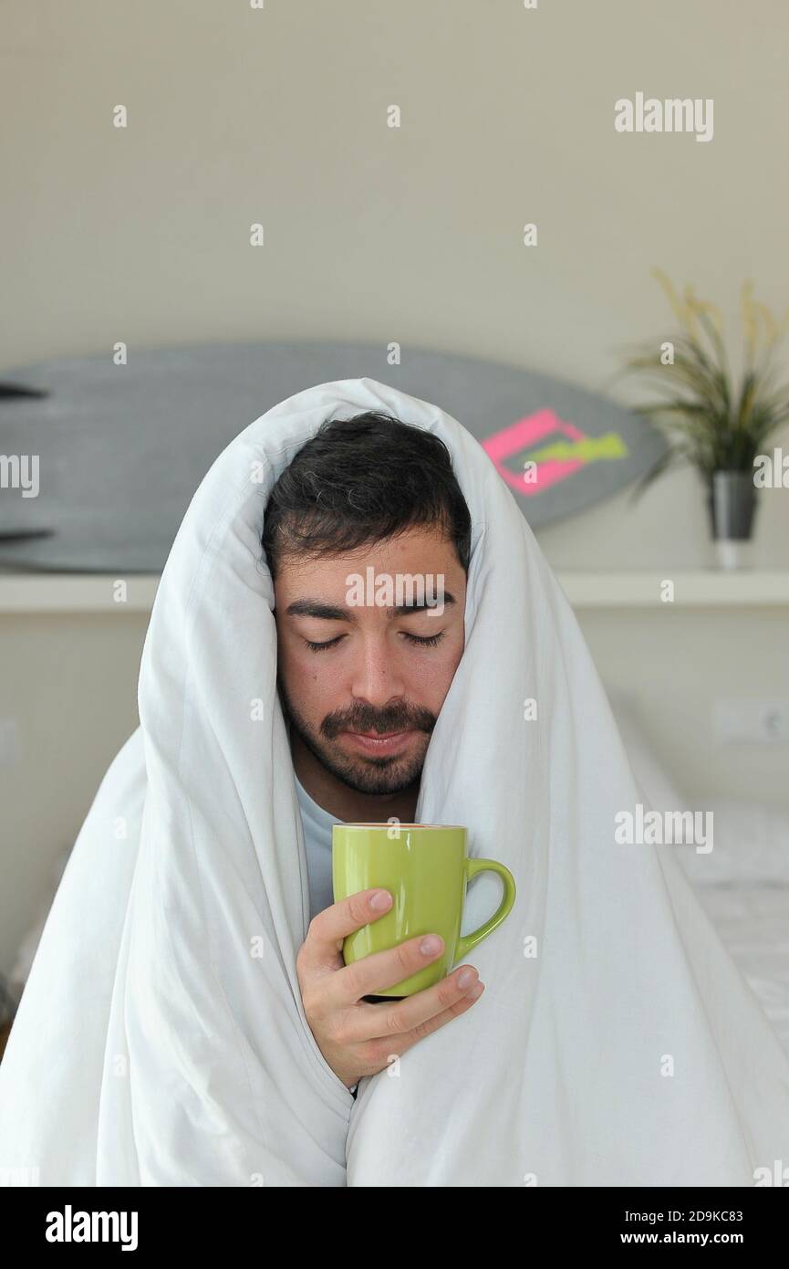 Man under blanket drinking coffee. Lockdown concept Stock Photo Alamy