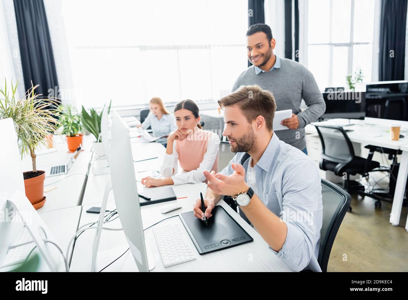 Businessman using graphics tablet and computer near multicultural colleagues in office Stock Photo