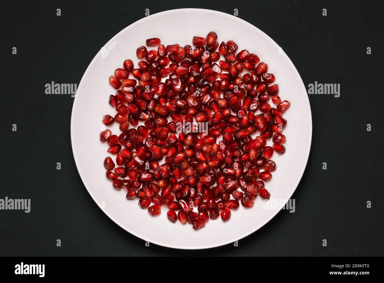 Pomegranate seeds on a plate isolated on a black background. Peeled fresh pomegranate. Healthy healthy food with vitamins Stock Photo