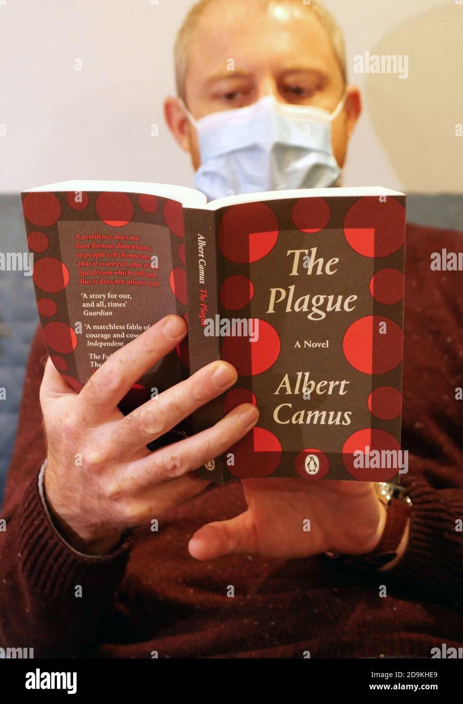 Man reads copy of The Plague by Albert Camus while wearing a facemask, London Stock Photo