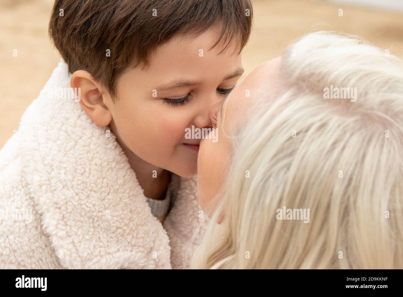 little boy tenderly kisses his mother on the sand in autumn in warm clothes. Family values. Single parent Stock Photo