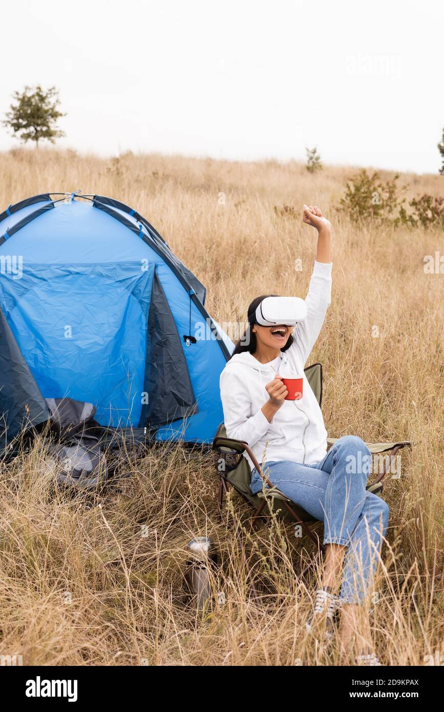 Cheerful african american woman in vr headset holding cup during camping  near tent on meadow Stock Photo - Alamy
