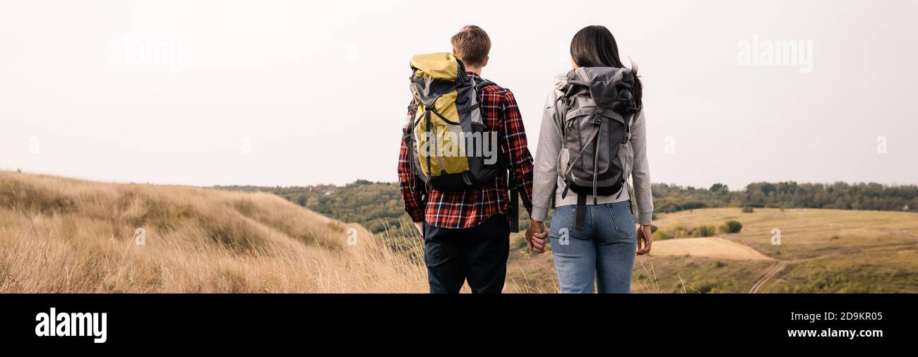Back view of multiethnic couple with backpacks holding hands while ...