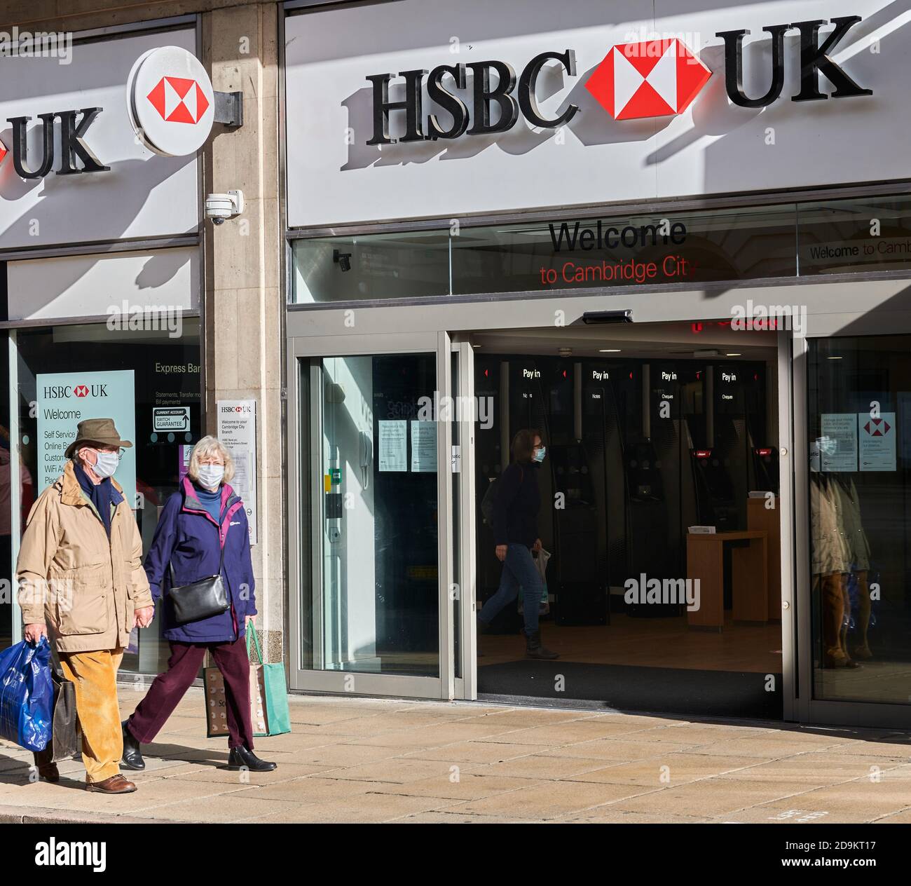 A couple wearing face masks pass the entrance to the branch of HSBC bank, Cambridge, England, during the coronavirus crisis, November 2020. Stock Photo