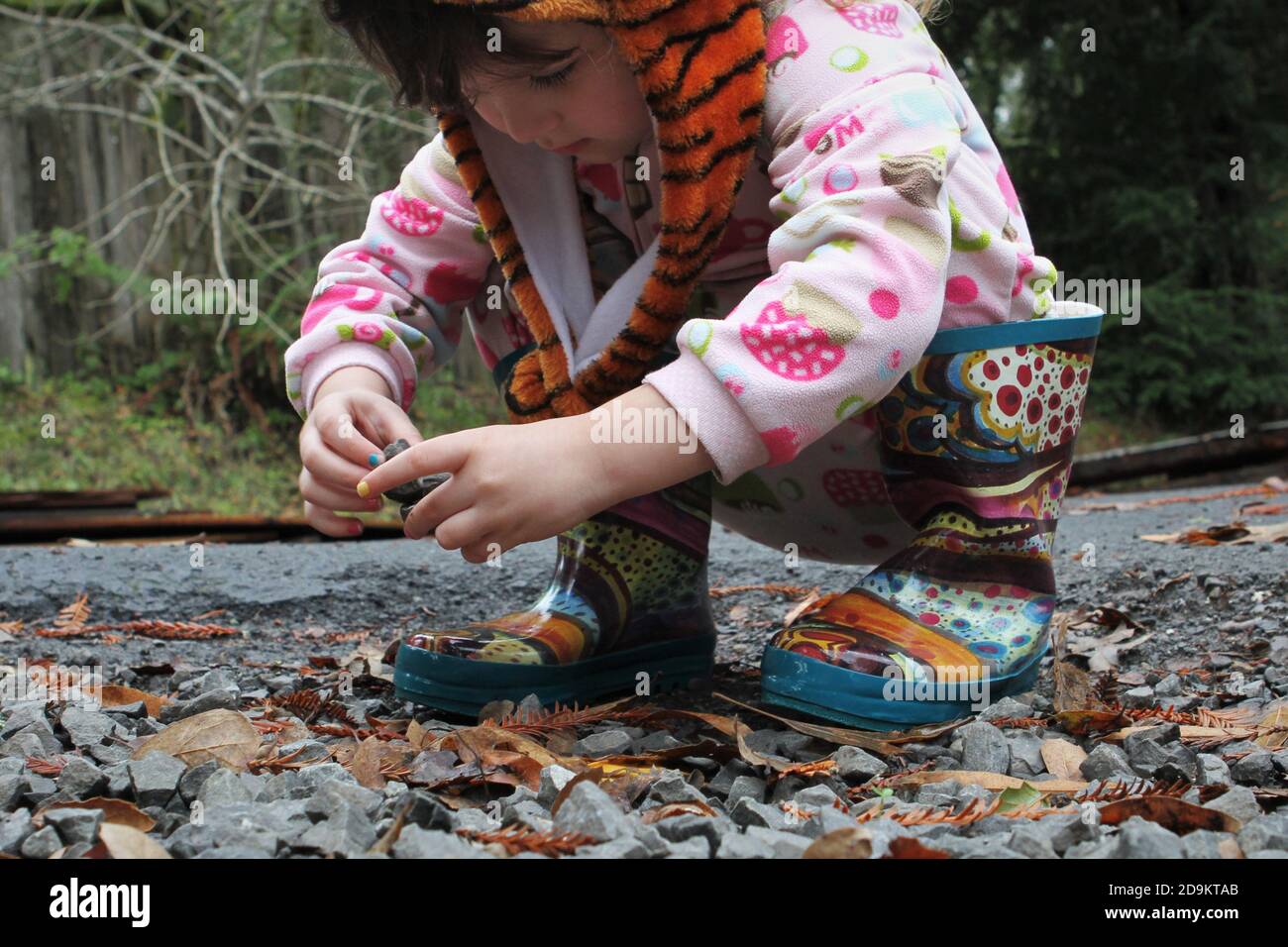 A young girl crouched and looking at rocks and other things on the ground. Stock Photo