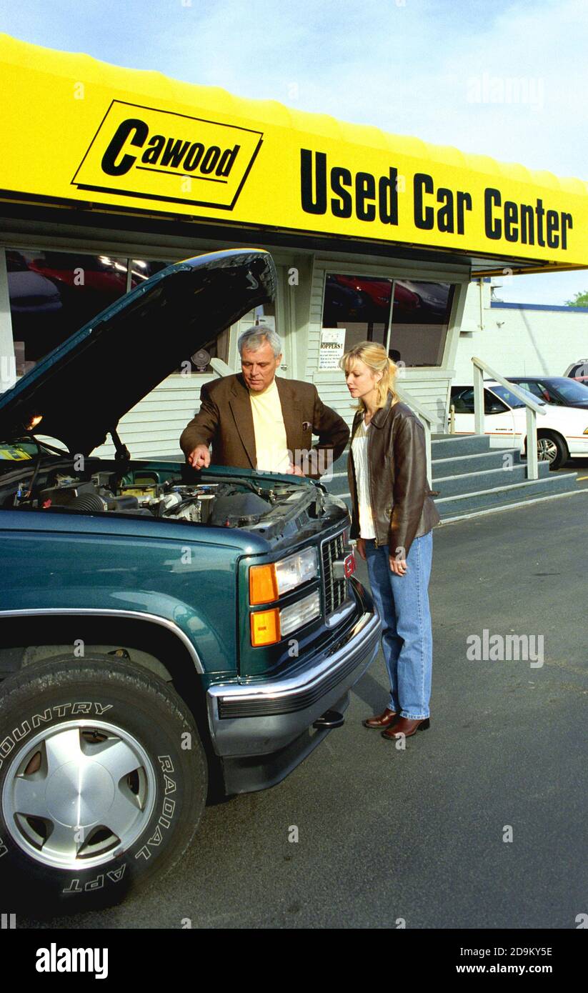 College age female shops for a used automobile and looks at the sticker price of the car on a used car lot Stock Photo