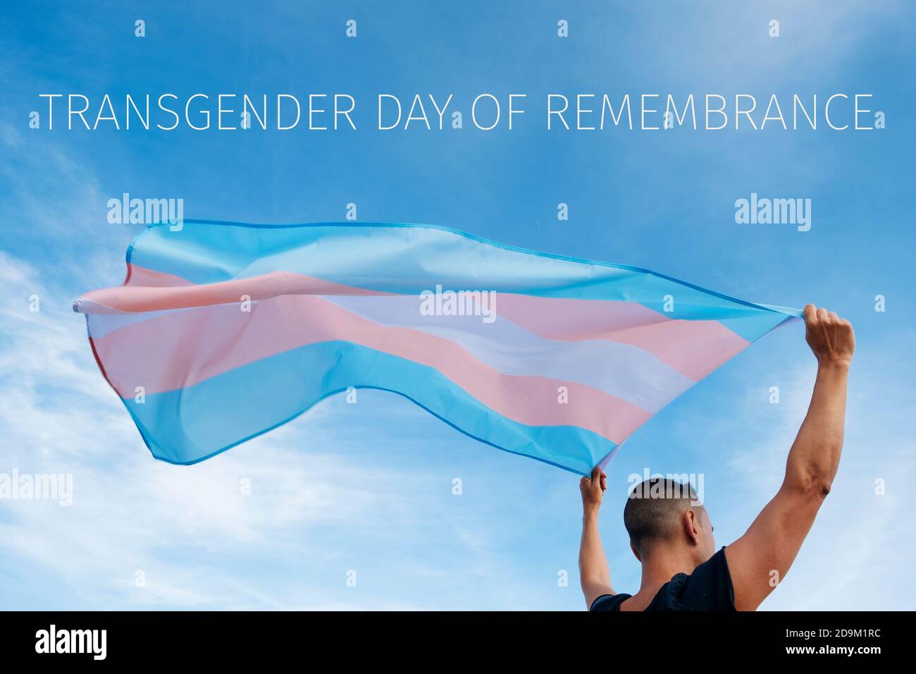 closeup of a young caucasian person, seen from behind, holding a transgender pride flag on the air and the text transgender day of remembrance on the Stock Photo