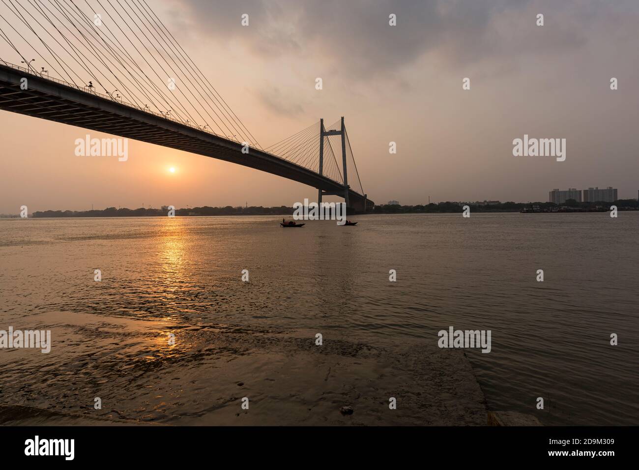 View of the famous Vidyasagar Setu against the backdrop of setting sun, boats on Hoogly river. Stock Photo