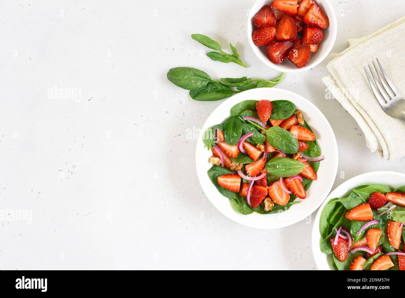 Fruit salad with strawberry, basil and walnut on light background with copy space. Fresh strawberries slices in  bowl. Top view, flat lay. Stock Photo
