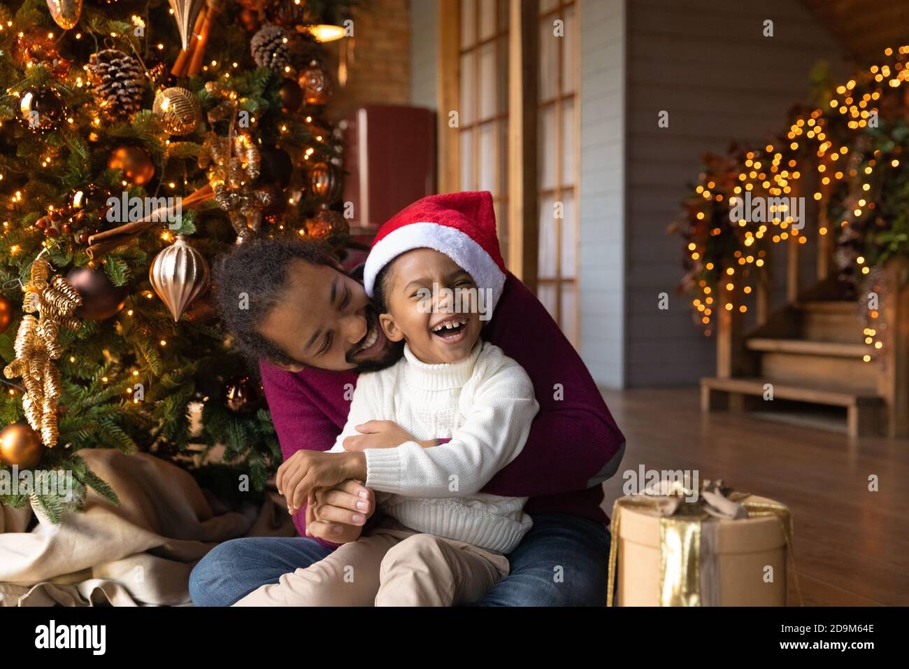 Overjoyed African American man hugging son, celebrating Christmas, opening gifts Stock Photo