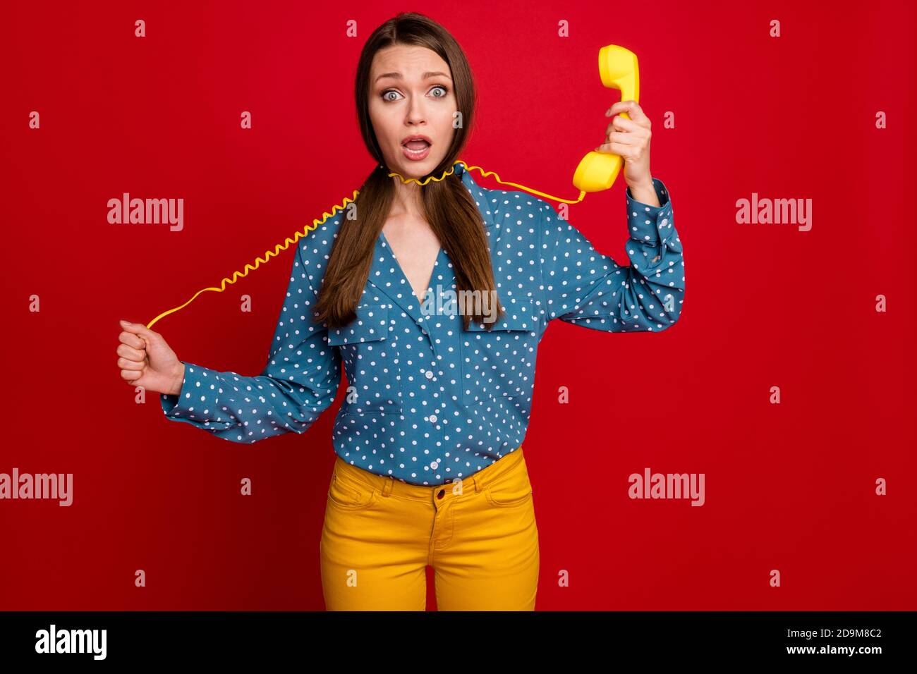 Portrait of pretty desperate girl holding in hand handset receiver strangling herself isolated on bright red color background Stock Photo
