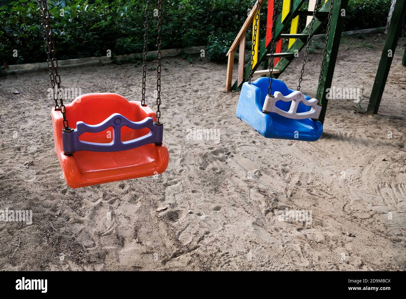 Empty swings on kindergarten playground. Unattended colorful swing set during coronavirus outbreak. Closed for children in pandemic. Nobody playing Stock Photo