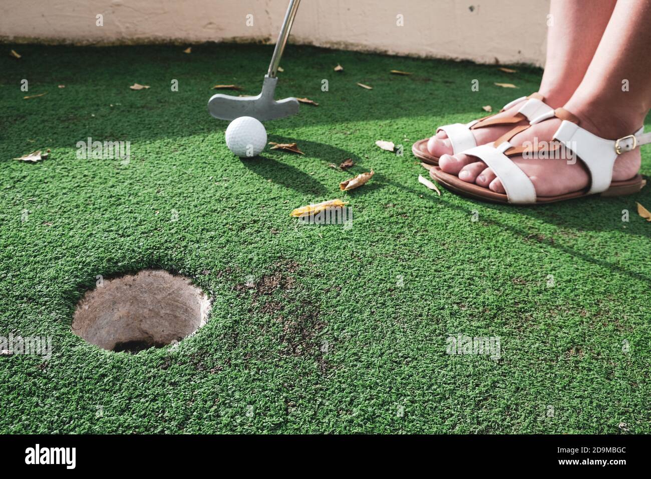 Girl or young woman playing mini golf on artificial green grass outdoors. Fun vacation entertainment for summertime. Putting club at ball, golf course Stock Photo