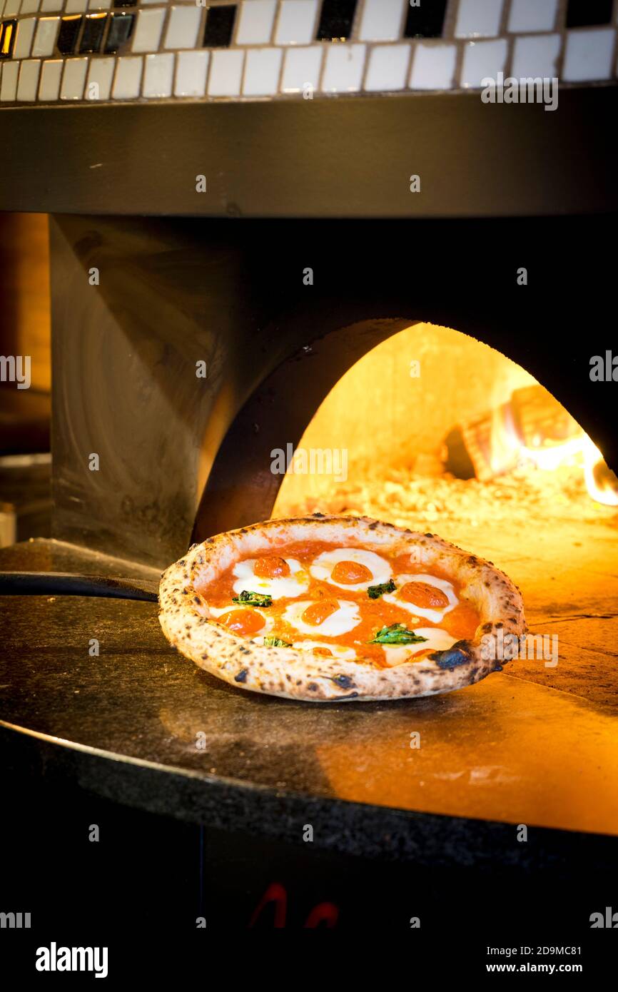 Margarita Pizza being pulled out of an open flame pizza oven Stock Photo