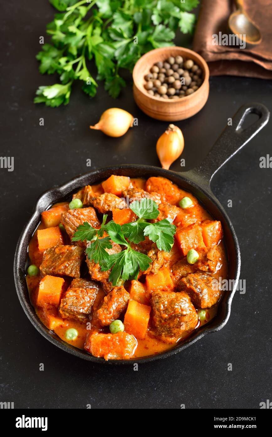 Beef stew with potatoes and carrots in tomato sauce on black stone background Stock Photo