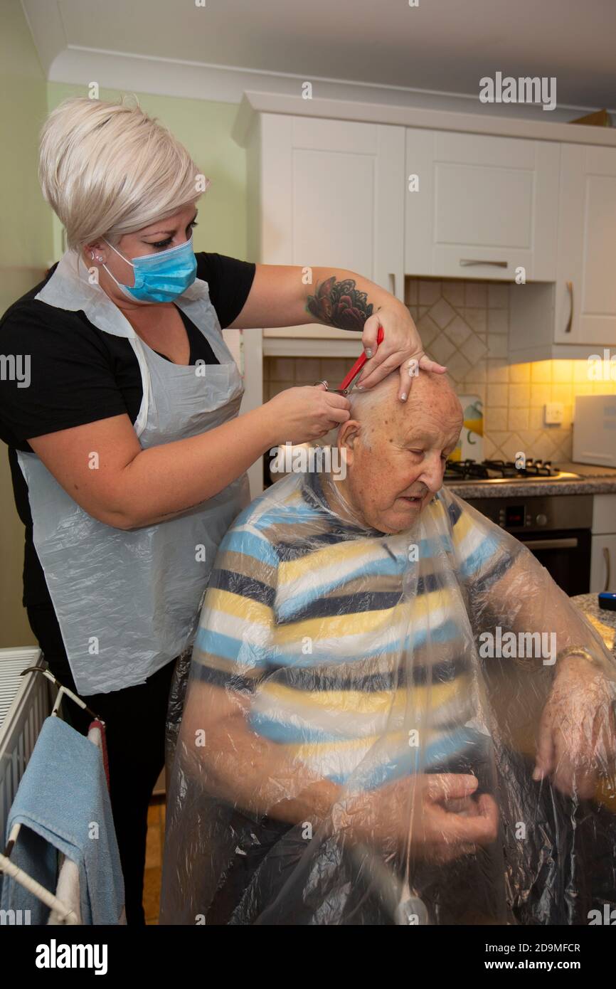 Elderly man in his eighties having his hair cut by a hairdresser wearing PPE as protection against coronavirus whilst at working remotely, England, UK Stock Photo