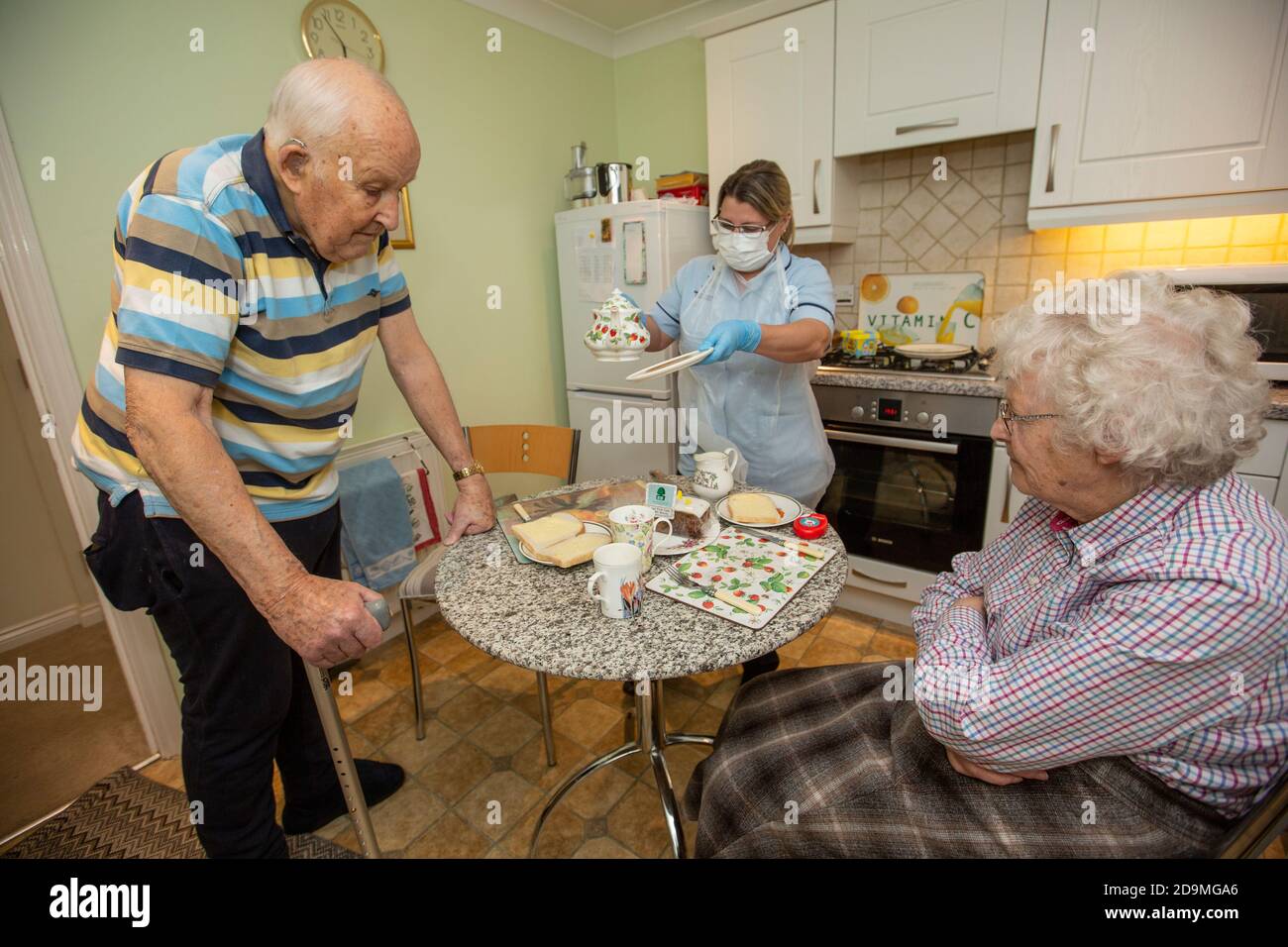 Elderly couple in their 80's at their home having tea served by a social care worker during the coronavirus pandemic lockdown, England, United Kingdom Stock Photo