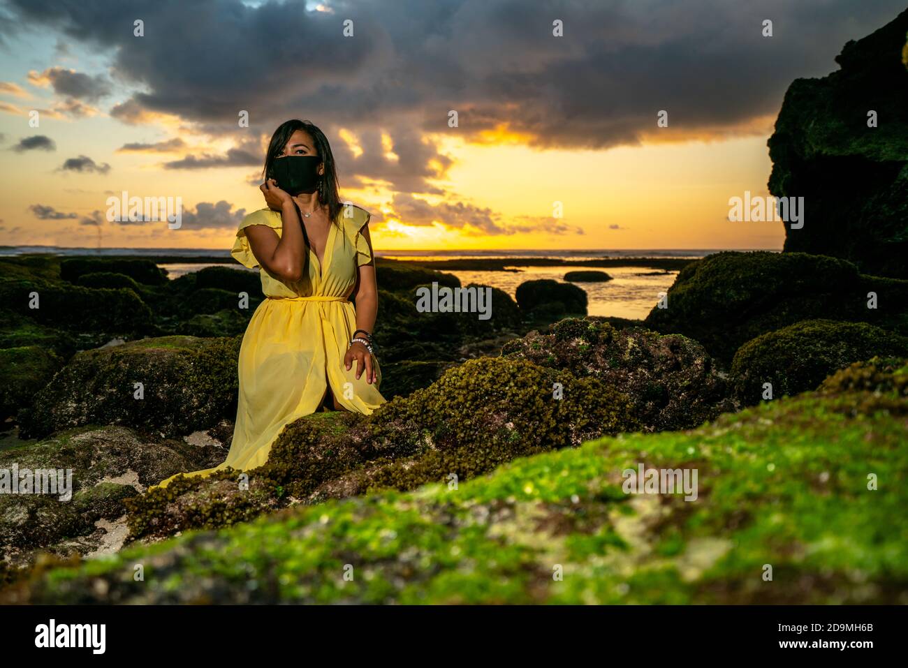 Beautiful Asian woman on beach in Bali at sunset wearing covid corona mask Stock Photo