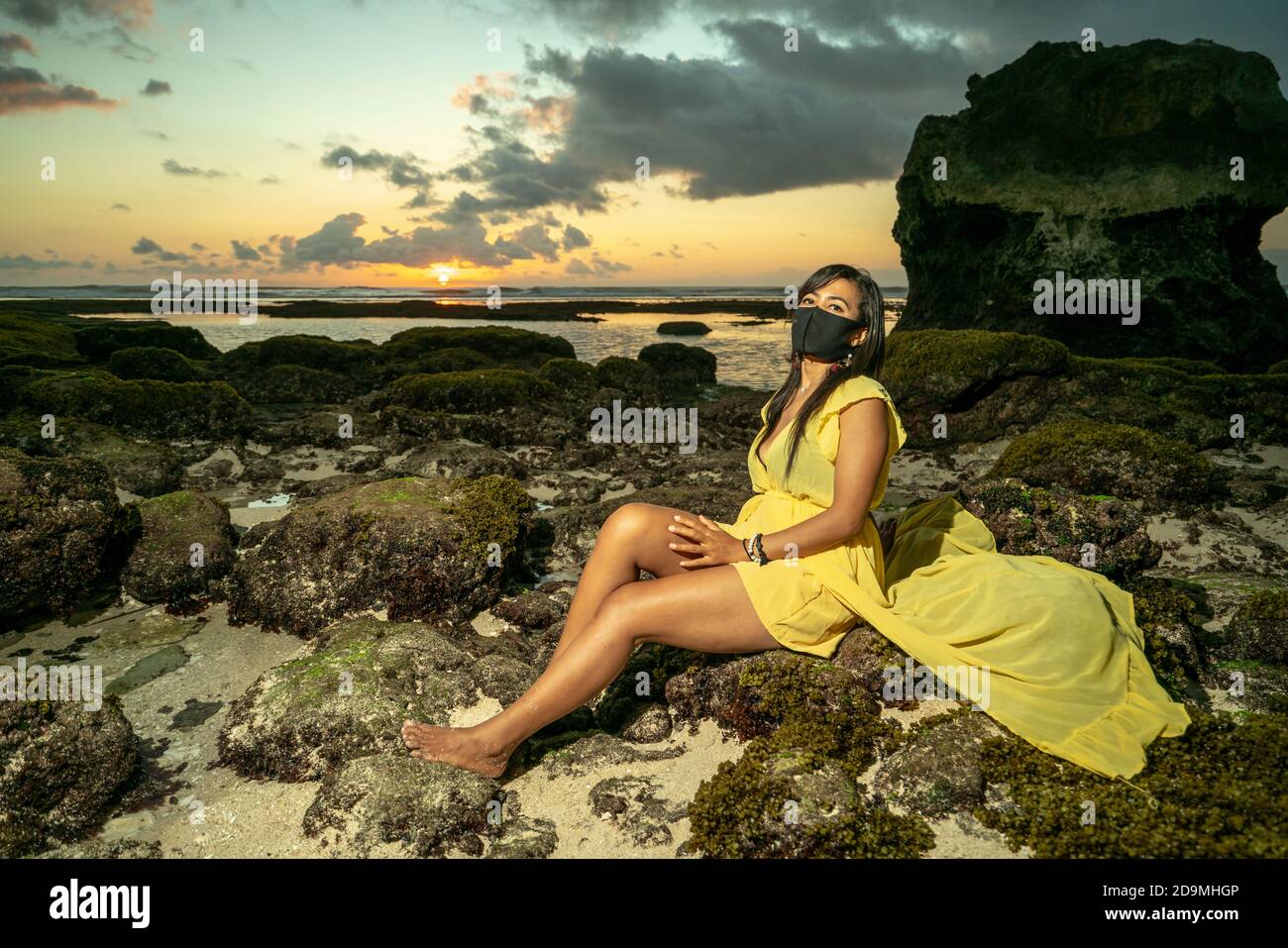 Beautiful Asian woman on beach in Bali at sunset wearing covid corona mask Stock Photo
