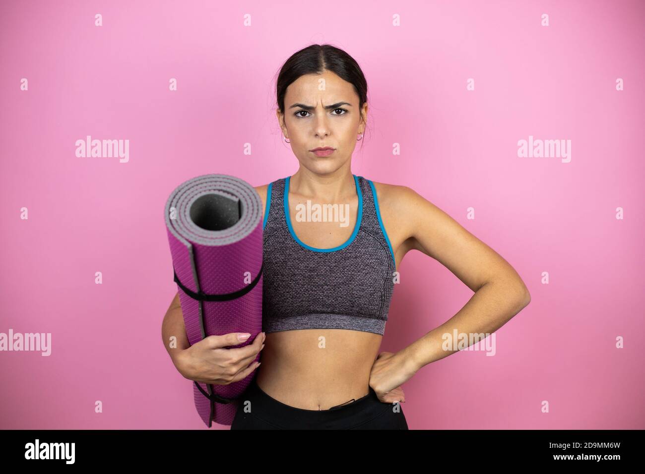 Young beautiful woman wearing sportswear over isolated pink background skeptic and nervous, disapproving expression on face with arms in waist. Holdin Stock Photo