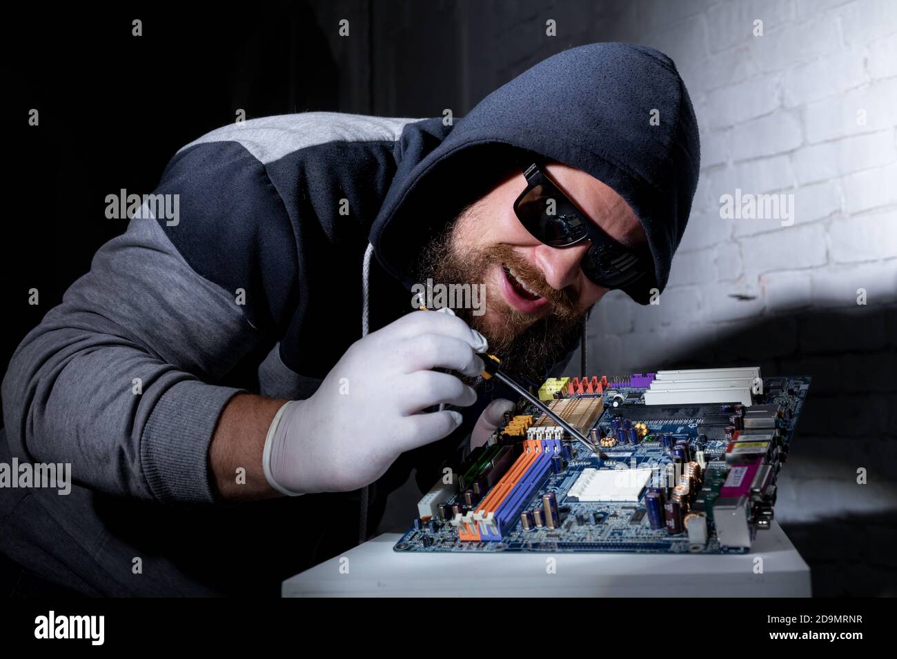 Bearded hacker in sunglasses and hoodie cracking the hardware studio