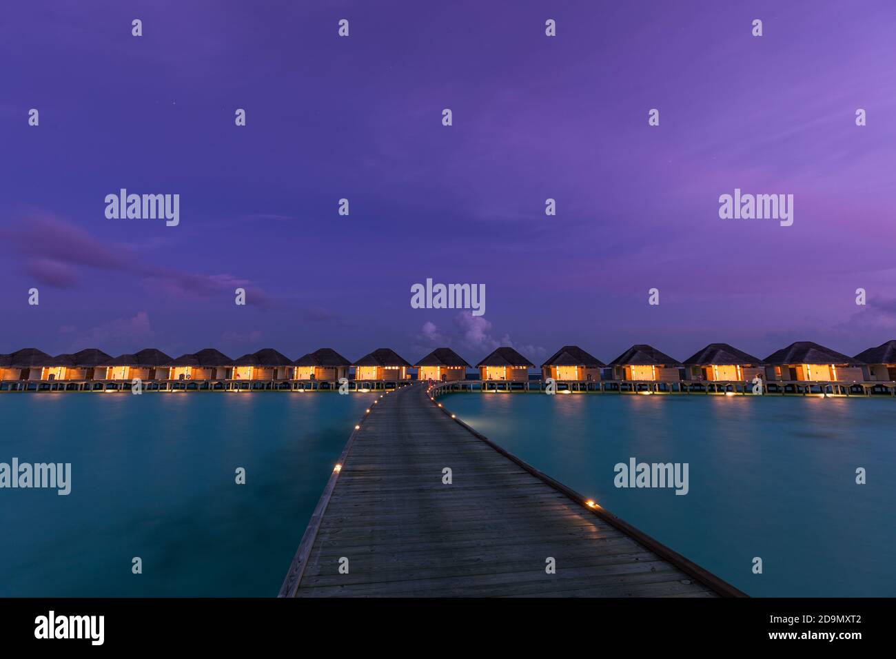 Overwater bungalows in Maldives islands. Tropical paradise island destination, led lights with long jetty under twilight night sky. Exotic landscape Stock Photo