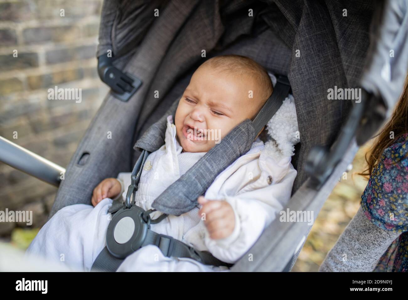 Distressed baby cries with eyes closed in a gray stroller next to a