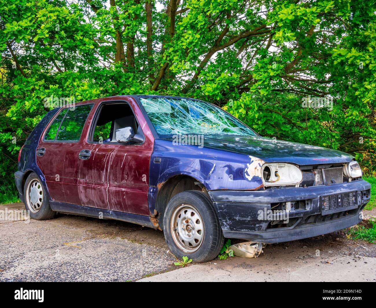 An abandoned car wreck with broken windows in the edge of parking lot