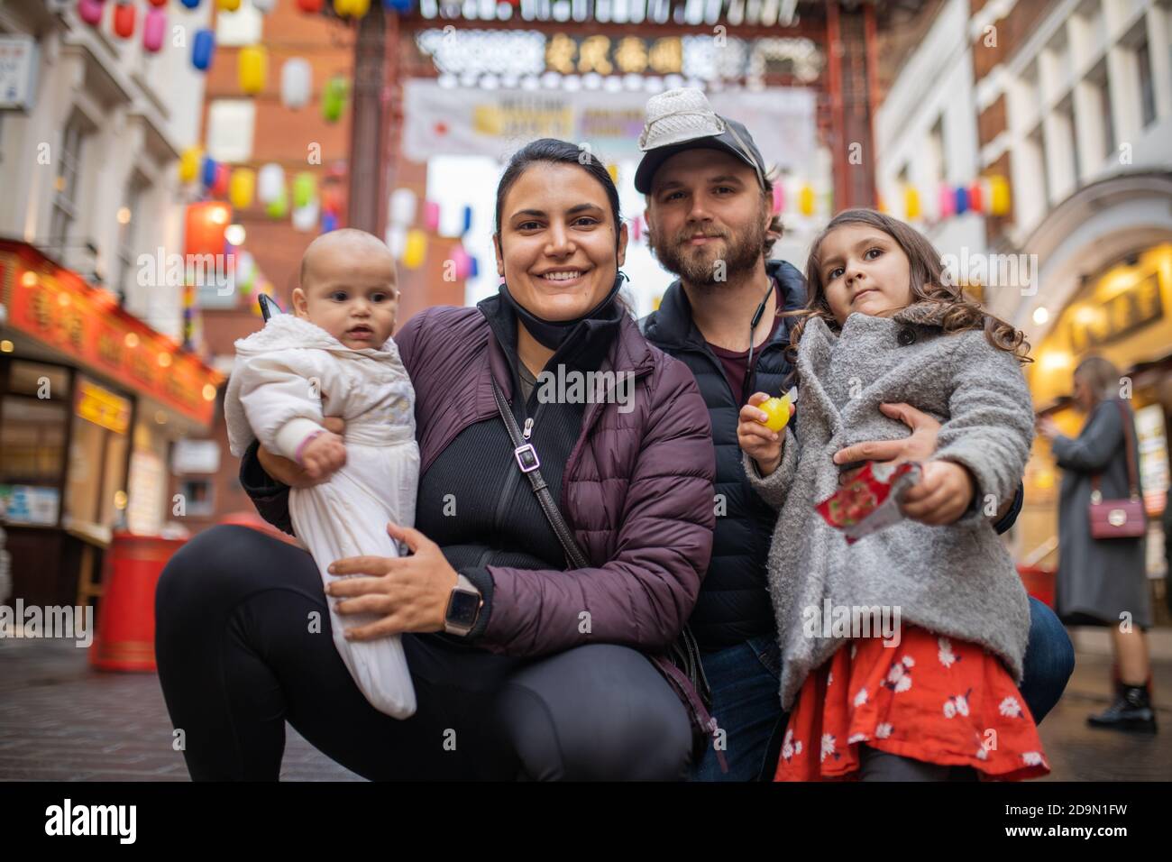 Two happy parents and their two daughters posing in a blurry Chinatown alley Stock Photo