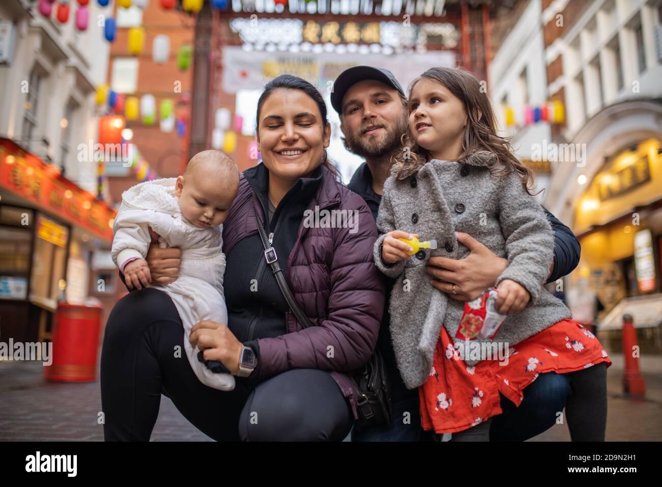 Two happy parents and their two daughters posing in a blurry Chinatown alley Stock Photo