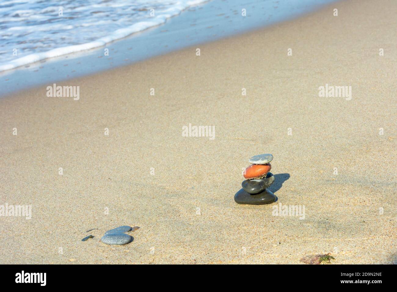 Stones are stacked in pyramid on the sand near sea. Harmony and meditation concept. Copy space, selective focus. Stock Photo