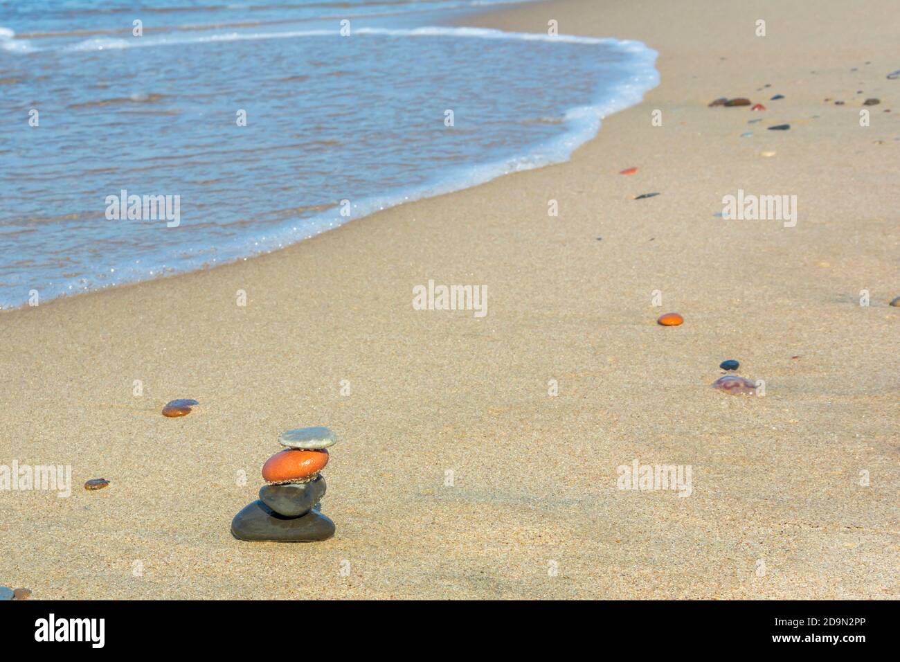 Pyramid of stones on seashore. Sandy beach sea water. Harmony and meditation concept. Copy space, selective focus. Stock Photo