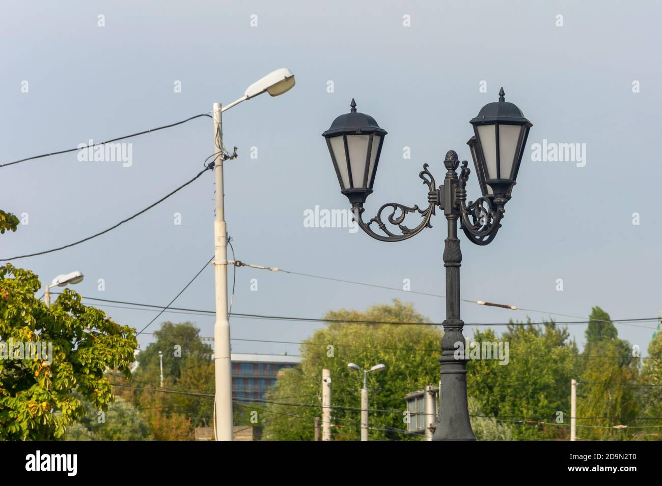 Retro street lamp with forged iron elements next to modern urban lighting pole. Concept of past and present, comparison, technology development. Stock Photo