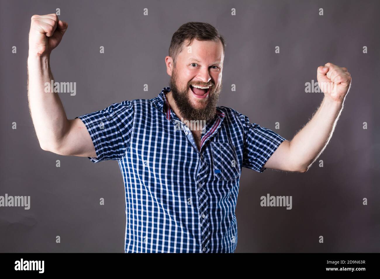 Joyful bearded man in shirt is happy to win emotional studio portrait ...