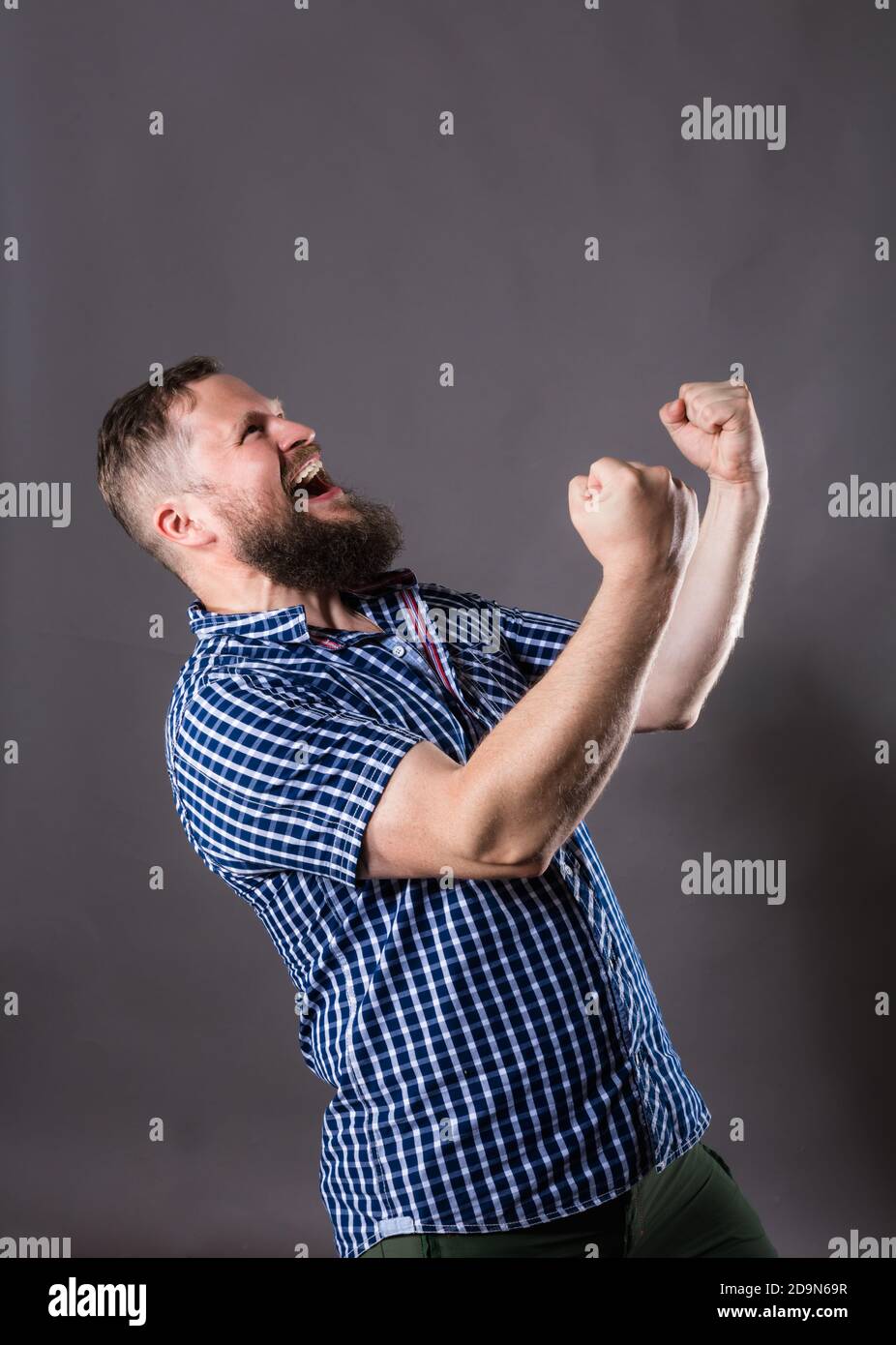 Joyful bearded man in shirt is happy to win emotional studio portrait ...