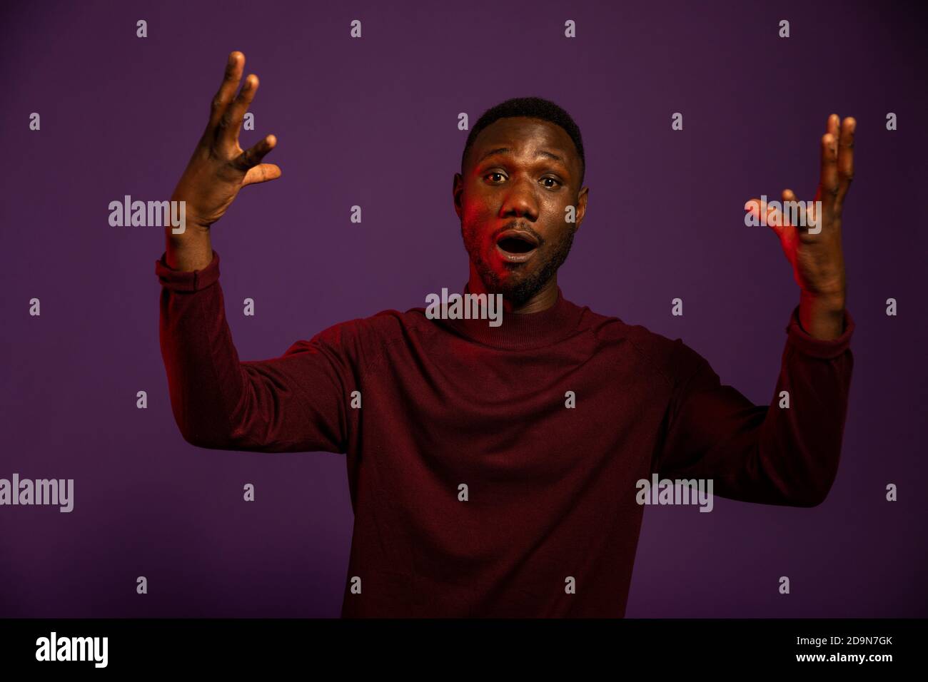 Black man with arms raised in surprise. Body language and facial expression. Medium shot. Isolated background. Looking at camera. Stock Photo