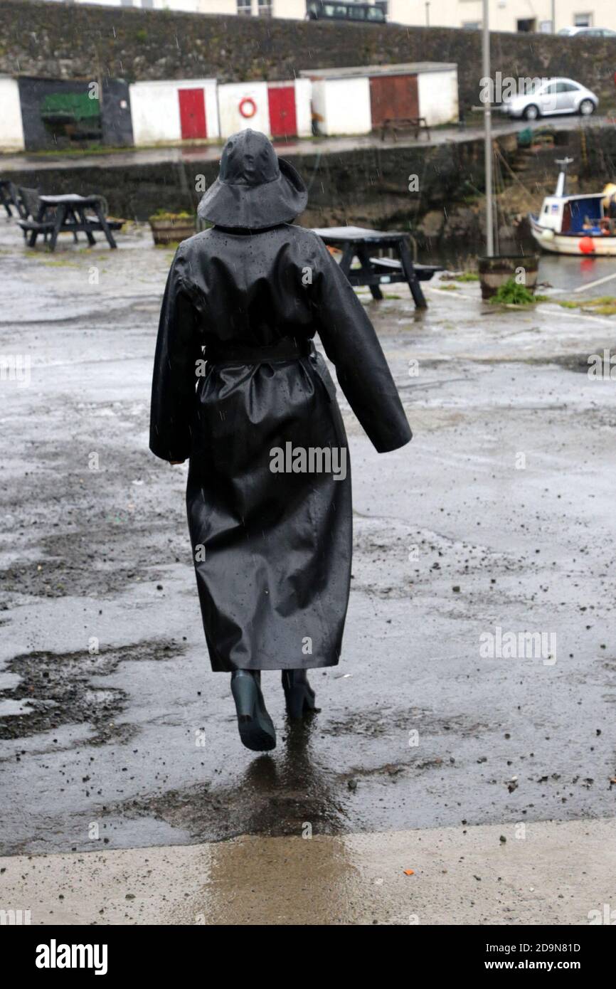 Mature white caucasian woman in designer rainwear, enjoying the rain and  outdoors. Shiny black rubber raincoat