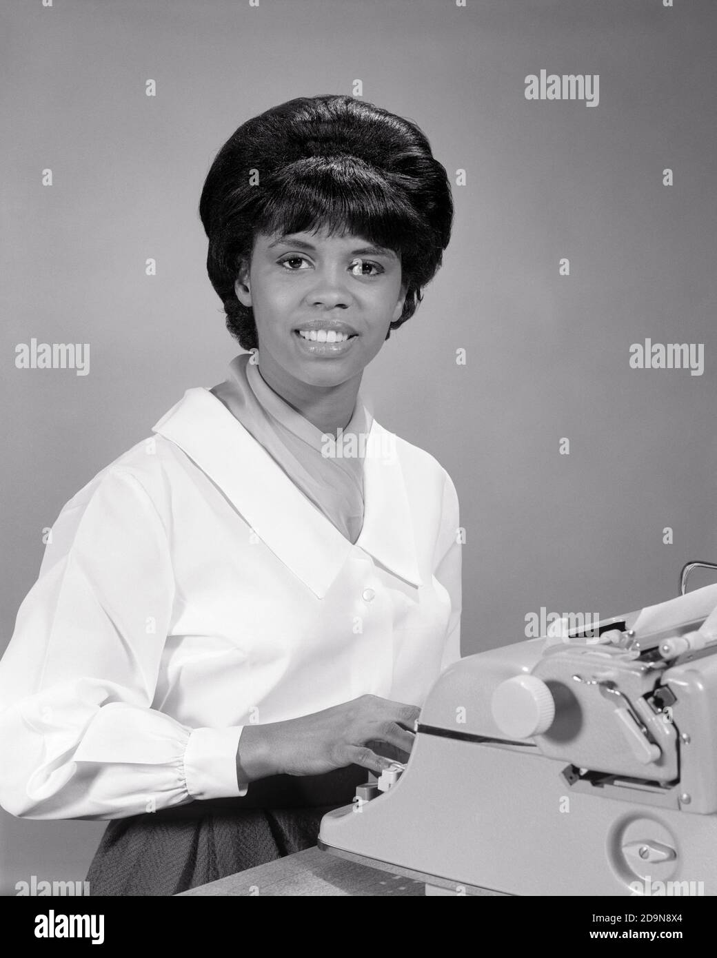 1960s AFRICAN-AMERICAN WOMAN AT ELECTRIC TYPEWRITER IN OFFICE SMILING LOOKING AT CAMERA - n2036 HAR001 HARS COPY SPACE HALF-LENGTH LADIES PERSONS PROFESSION CONFIDENCE B&W BUSINESSWOMAN SKILL OCCUPATION HAPPINESS SKILLS CHEERFUL CUSTOMER SERVICE AFRICAN-AMERICANS AFRICAN-AMERICAN CAREERS BLACK ETHNICITY LABOR PRIDE OFFICE WORKER IN OPPORTUNITY EMPLOYMENT OCCUPATIONS SMILES GAL FRIDAY ADMINISTRATOR JOYFUL SECRETARIES BUSINESSWOMEN EMPLOYEE AMANUENSIS YOUNG ADULT WOMAN BLACK AND WHITE CLERICAL HAR001 LABORING OLD FASHIONED AFRICAN AMERICANS Stock Photo