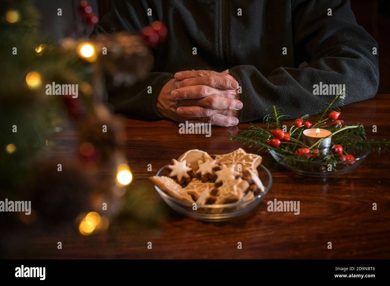 Praying hands of an elderly man on a table with Christmas cookies, burning candle and festive decoration, lonely holidays during the coronavirus pande Stock Photo