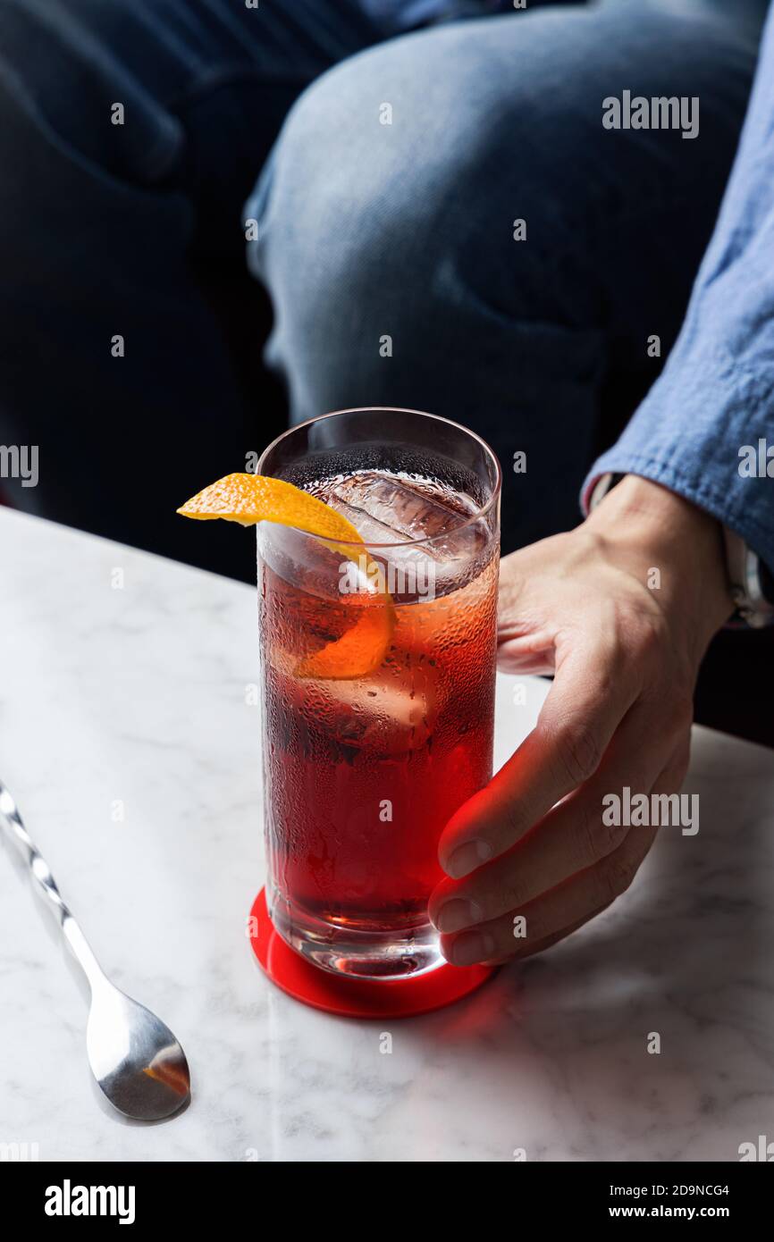 Man's hand grabbing Americano Cocktail with Orange Twist Stock Photo