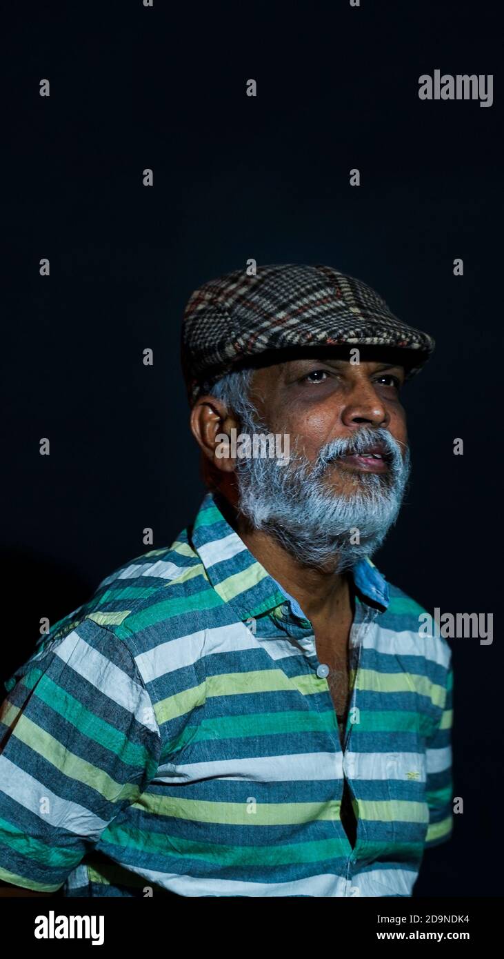 Vertical shot of a bearded Asian senior man wearing a stylish hat isolated on a black background Stock Photo
