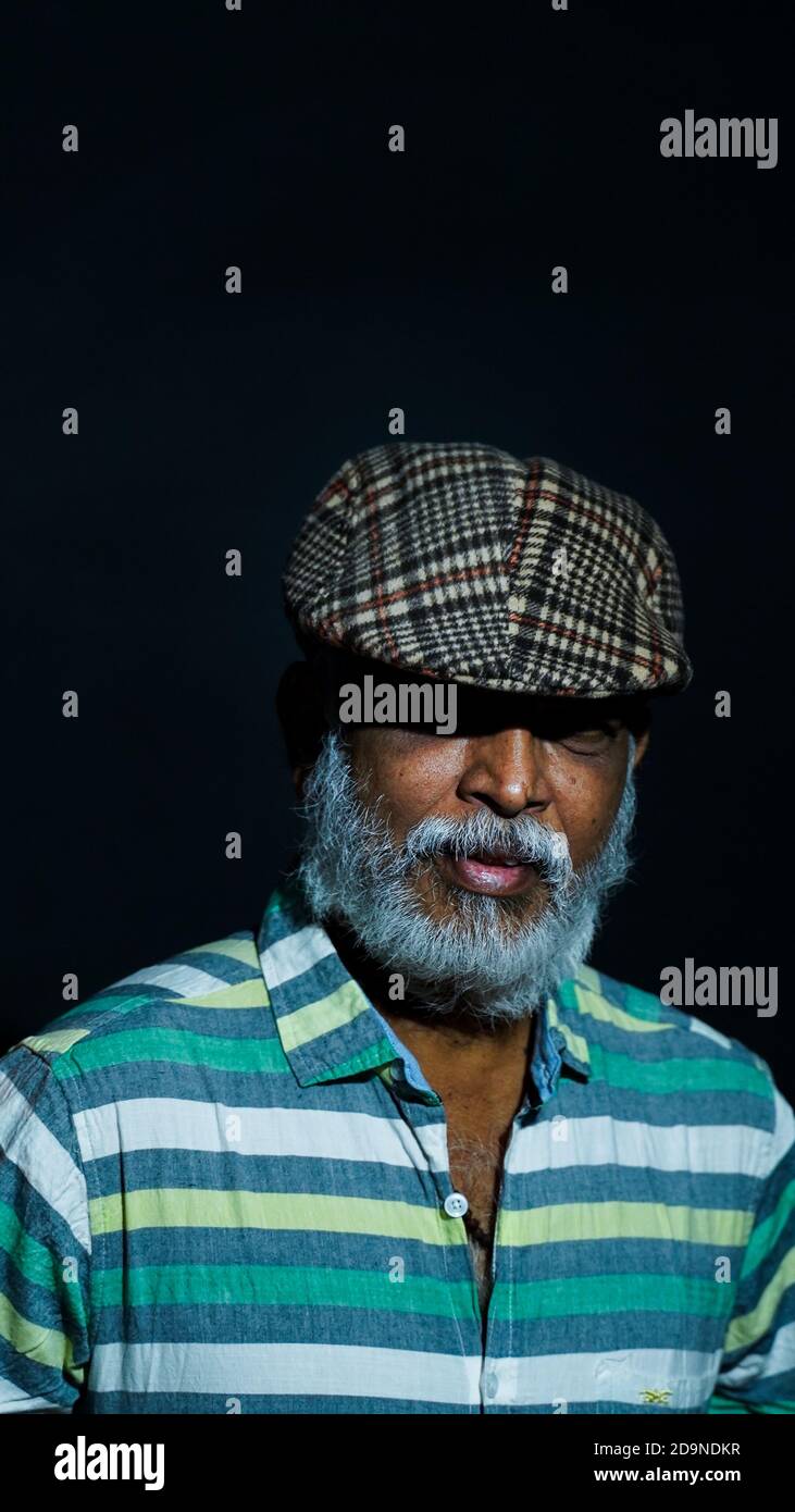 Vertical shot of a bearded Asian senior man wearing a stylish hat isolated on a black background Stock Photo