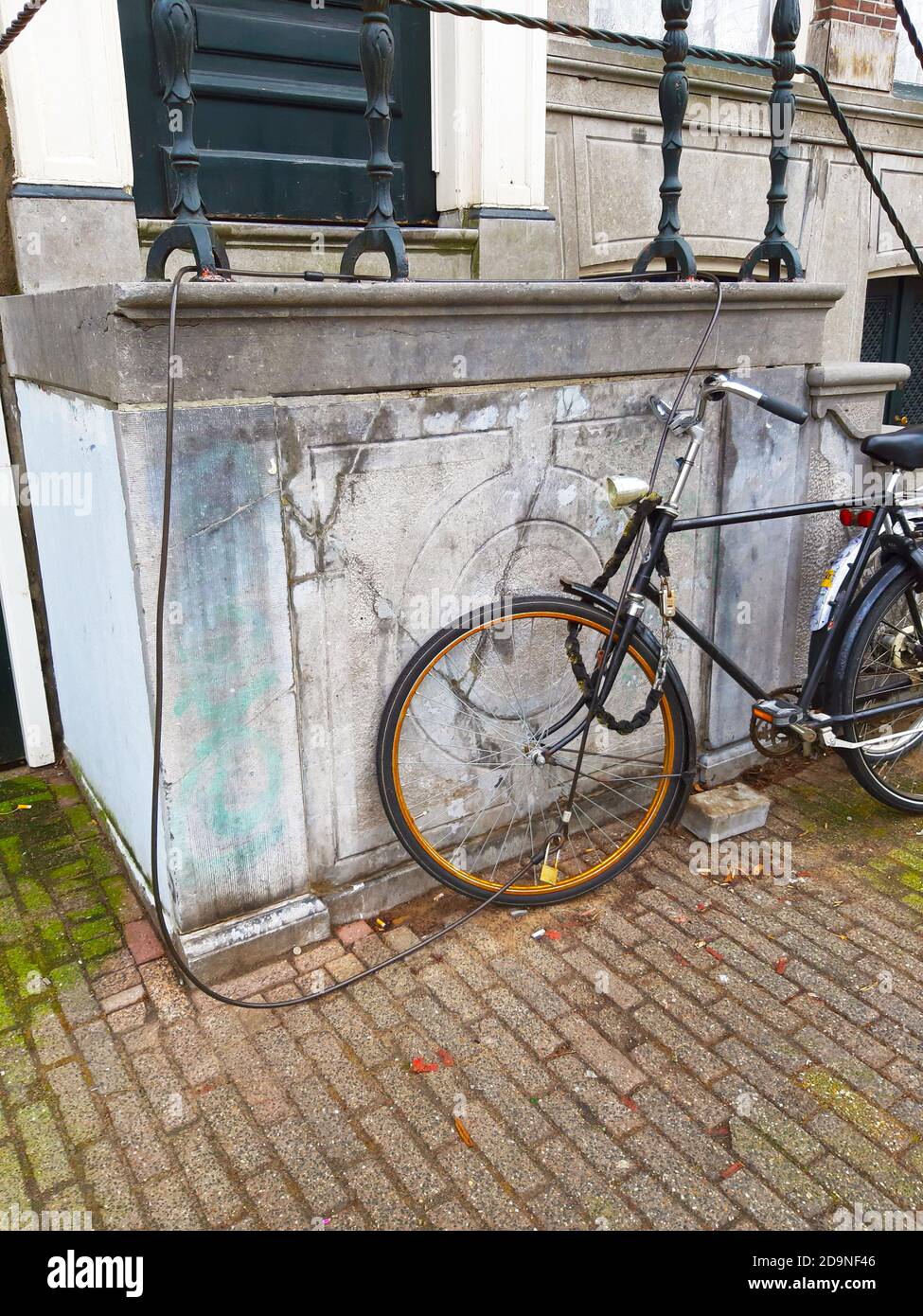 Dutch bicycles parked abandoned on the wall of a house with the anti theft security chain along the sidewalk in amsterdam netherlands holland Stock Photo