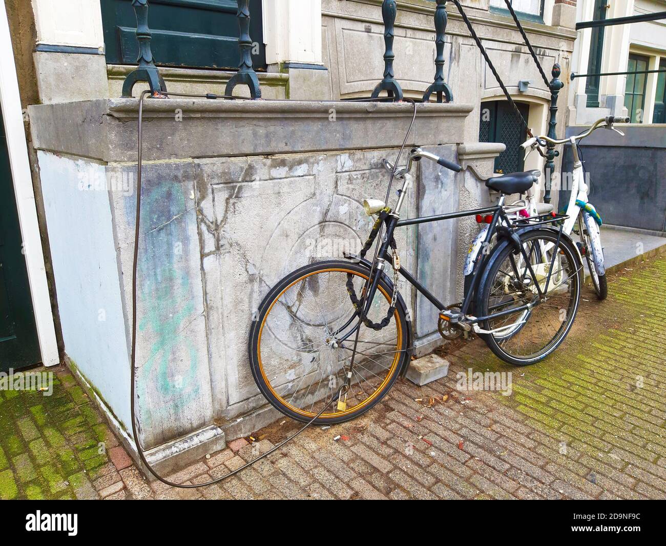 Dutch bicycles parked abandoned on the wall of a house with the anti theft security chain along the sidewalk in amsterdam netherlands holland Stock Photo