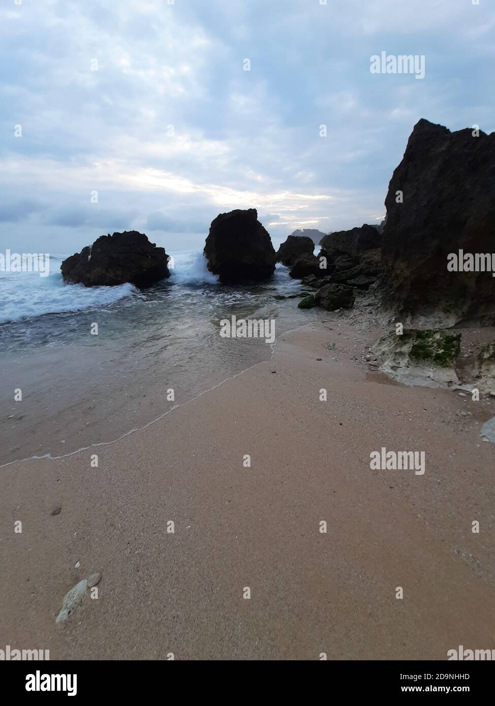 Single rocks on a sand beach against blue ocean and cloud sky at ...